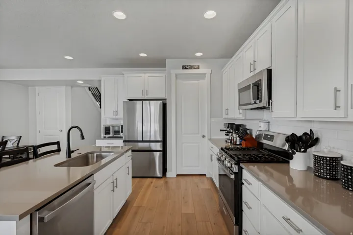 Kitchen featuring white cabinetry, stainless steel appliances, wood-finish flooring, light-toned countertops, and a subway tile backsplash