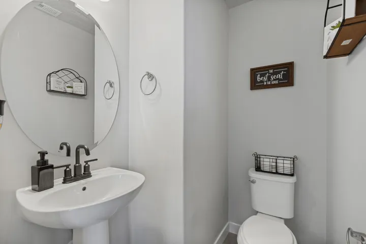 Pedestal sink with a matte black faucet, wall-mounted oval mirror, and a white toilet