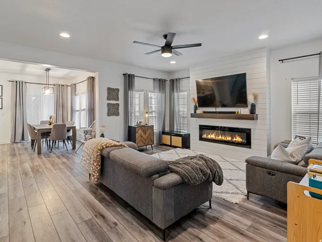 Light wood-finish flooring, recessed lighting, and a ceiling fan are featured in this open-concept living area