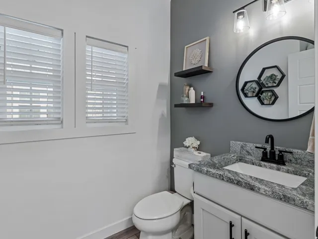 Vanity with a stone-finish countertop and undermount sink, matte black faucet, and wood-finish flooring