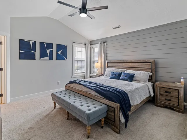 Vaulted ceiling with a ceiling fan, shiplap accent wall, two windows with blinds, and carpet flooring