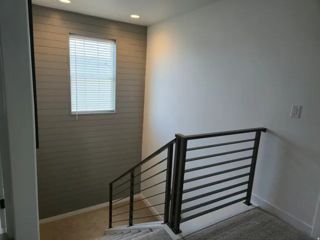 Modern horizontal metal railing with carpeted stairs, shiplap accent wall, recessed lighting, and a window with blinds