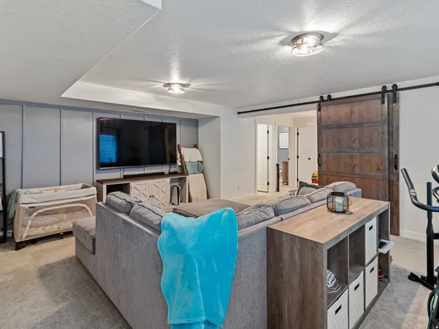 Recessed ceiling lighting, wood-finish entertainment console, accent wall paneling, dual barn doors, and carpet flooring