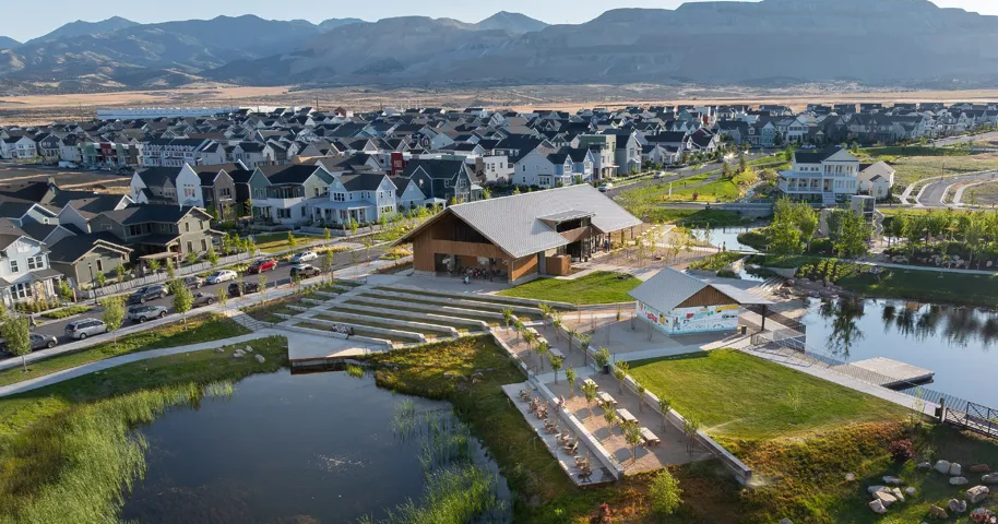 Community amenity center with a large gathering building, outdoor amphitheater seating, a covered pavilion, and a dock on a pond