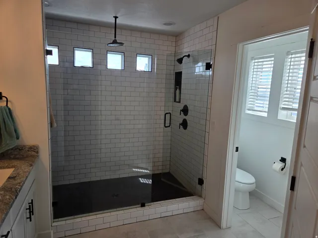 Walk-in shower with subway tile surround, glass enclosure, and black rain shower head