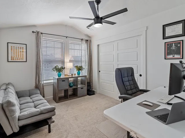 Vaulted ceiling with a black ceiling fan, dual windows with blinds, built-in shelving, and white paneled sliding closet doors