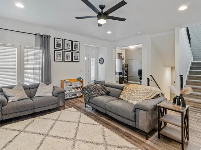 Recessed lighting throughout, wood-finish flooring, staircase with carpeted treads, ceiling fan with integrated lighting, and multiple windows with blinds