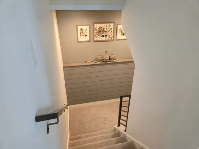 Carpeted staircase with a metal handrail, featuring an accent wall with shiplap paneling and a built-in display ledge
