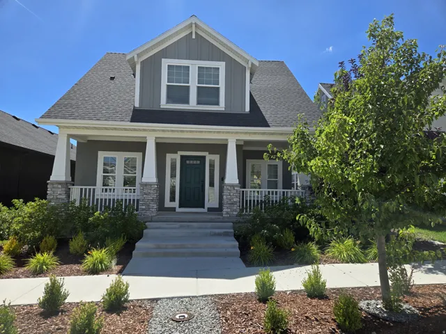 Two-story residence featuring a covered front porch with stone accents, a dark-paneled front door, and a light gray facade