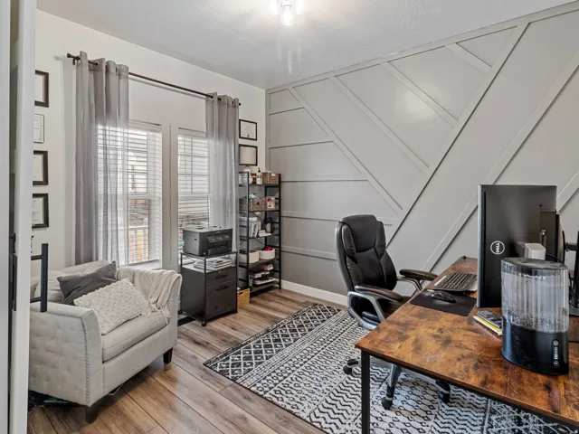 Room featuring wood-finish flooring, accent wall with geometric paneling, and two windows with blinds