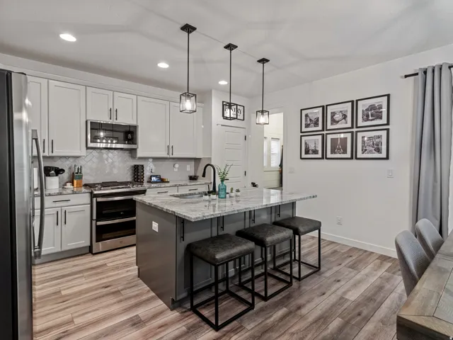 Kitchen featuring light-toned cabinetry, stainless steel appliances, a center island with counter seating, and wood-finish flooring