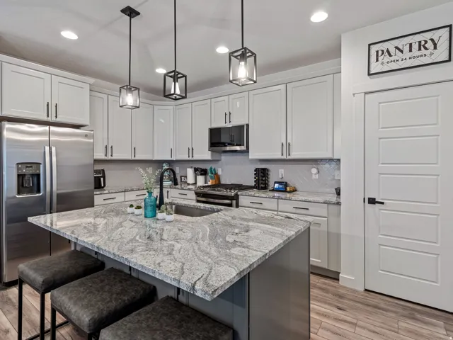 Kitchen featuring a large island with an integrated sink, stainless steel appliances, shaker-style cabinetry, and pendant lighting