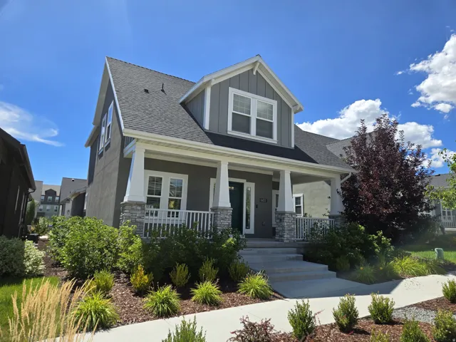 Two-story residence featuring a covered front porch with stone pillars, a dark gray shingle roof, and a mature ornamental tree