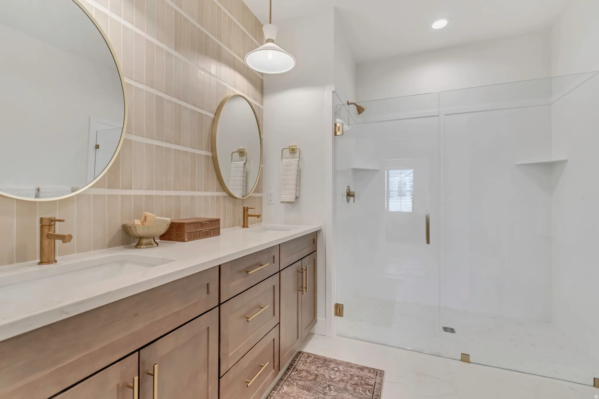 Dual vanity with integrated sinks, brushed gold fixtures, and light wood-finish cabinetry