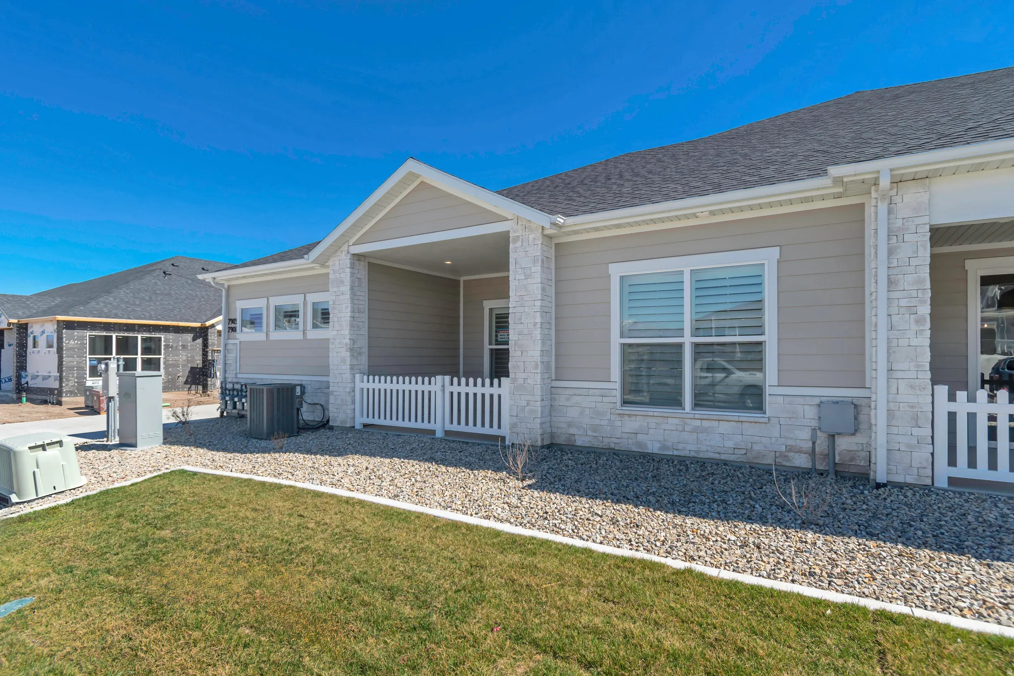 Outdoor patio with white picket fencing, light siding, stone facade, and a manicured lawn area