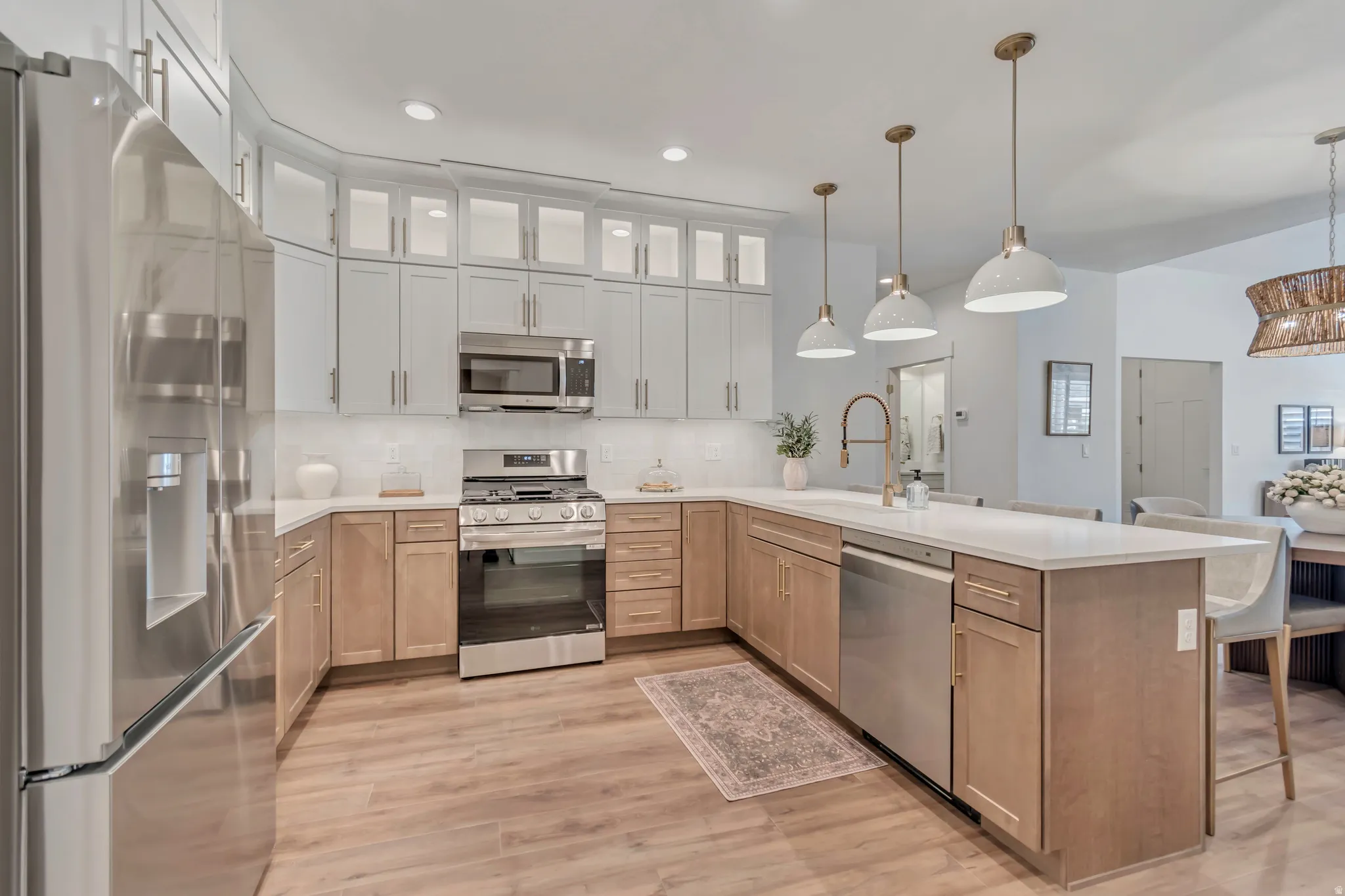 Contemporary kitchen featuring wood-finish flooring, two-tone cabinetry, stainless steel appliances, and a central island with pendant lighting
