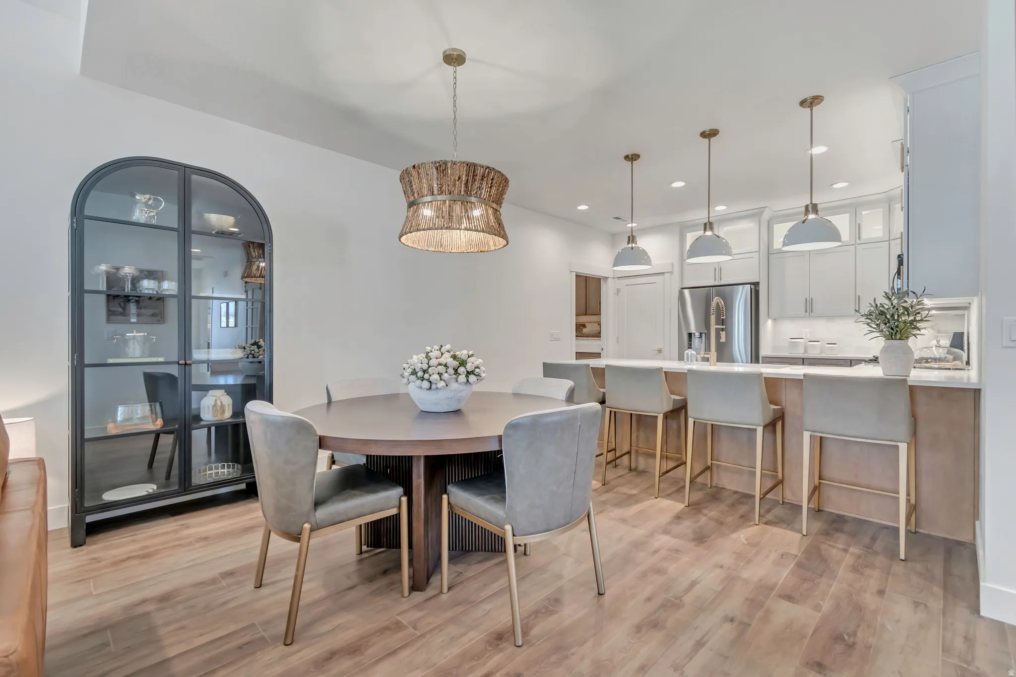 Open-concept living space featuring wood-finish flooring, a kitchen island with pendant lighting, white cabinetry, and stainless steel appliances
