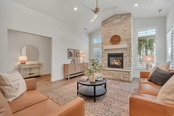 Vaulted ceiling, stone-clad fireplace with mantel, recessed lighting, ceiling fan, and wood-finish flooring