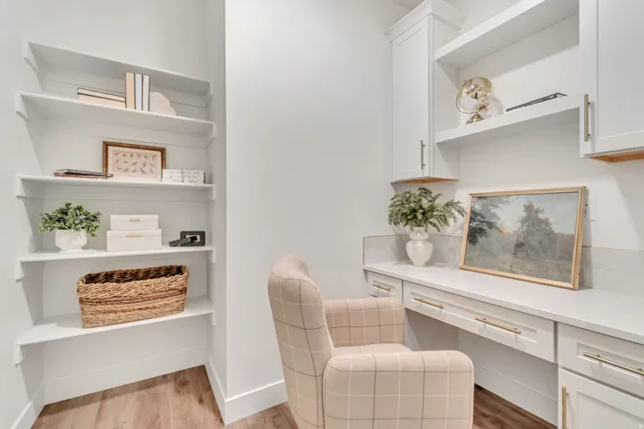 Built-in desk with a stone countertop and integrated cabinetry, complemented by open shelving and wood-finish flooring