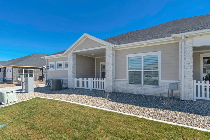 Outdoor patio with white picket fencing, light siding, stone facade, and a manicured lawn area