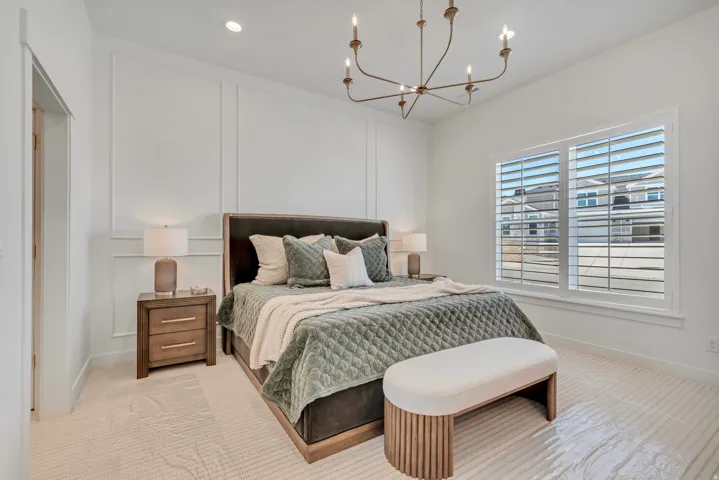 Recessed lighting, decorative wall paneling, a contemporary chandelier, large window with plantation shutters, and light-toned flooring