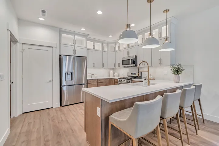 Wood-finish flooring, recessed lighting, stainless steel appliances, a kitchen island with a light-toned countertop, and pendant lighting