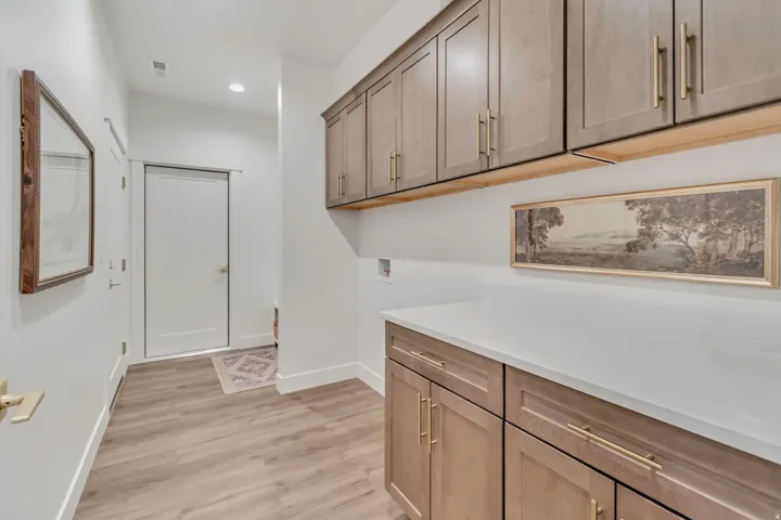 Built-in cabinetry with gold-toned hardware, white solid surface countertop, wood-finish flooring, and recessed lighting