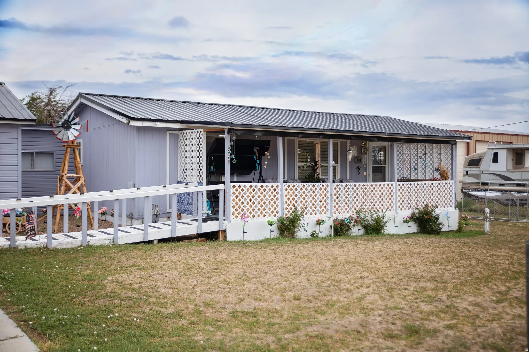 Exterior featuring light-colored siding, a dark metal roof, and a covered front porch with white lattice railing