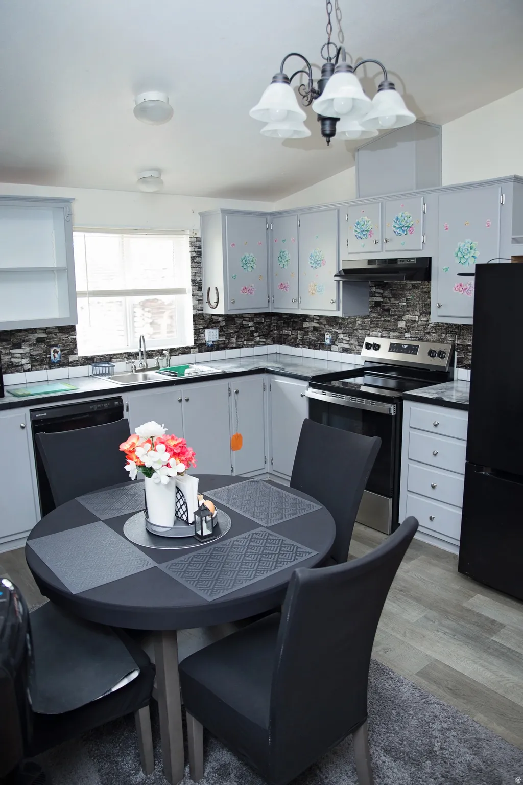 Kitchen featuring wood-finish flooring, dark stone-look backsplash, light cabinetry, stainless steel appliances, and a vaulted ceiling with a chandelier