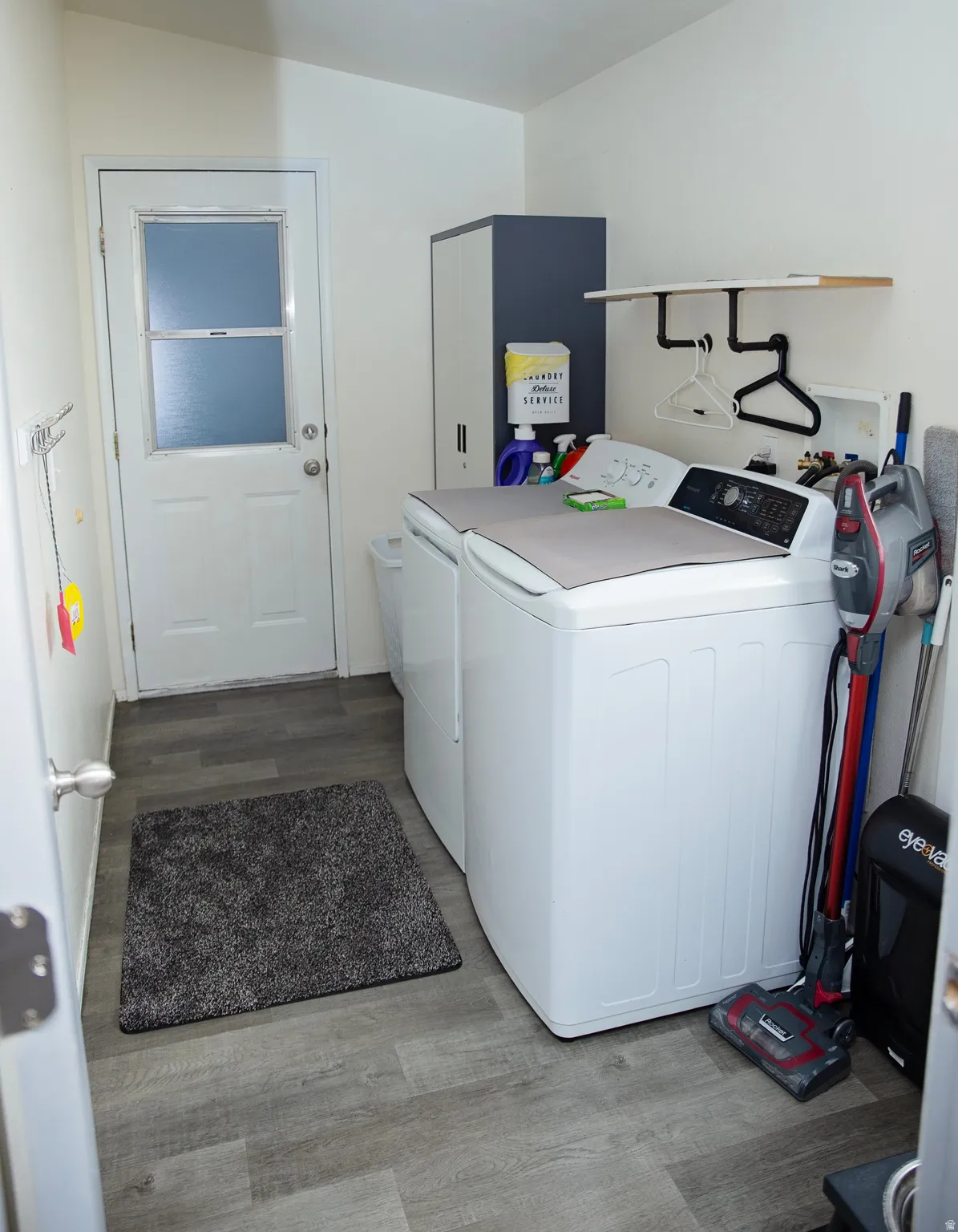 Laundry area featuring wood-finish flooring, white walls, and a built-in shelf