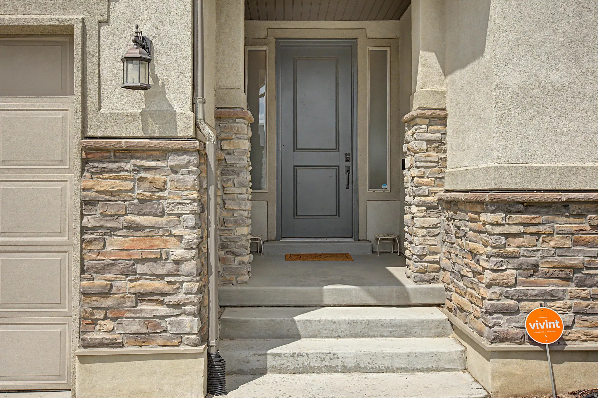 Exterior featuring stucco and stone veneer accents, a paneled entry door, a side light, and an exterior wall lantern