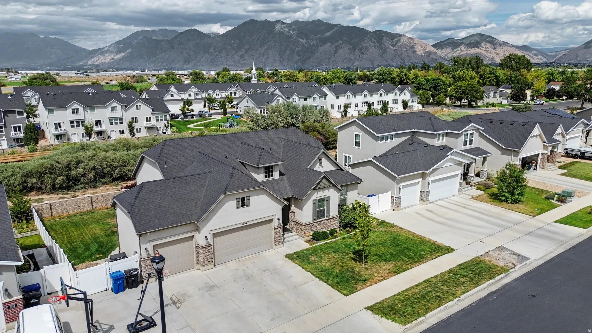Two-story residence with a multi-gabled roofline, light-toned stucco exterior, and stone veneer accents