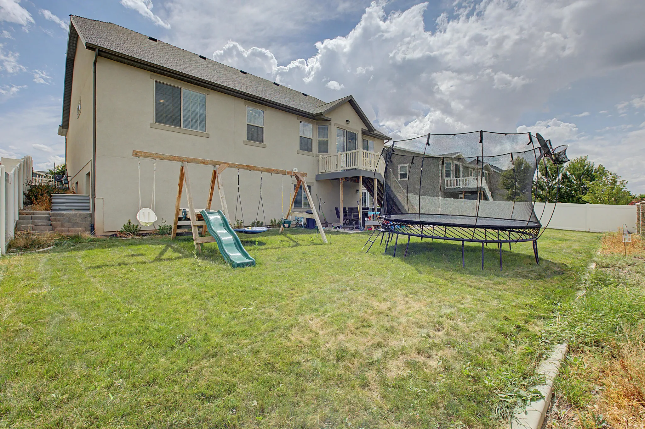 Expansive backyard featuring a stucco exterior, upper-level deck, and a privacy fence