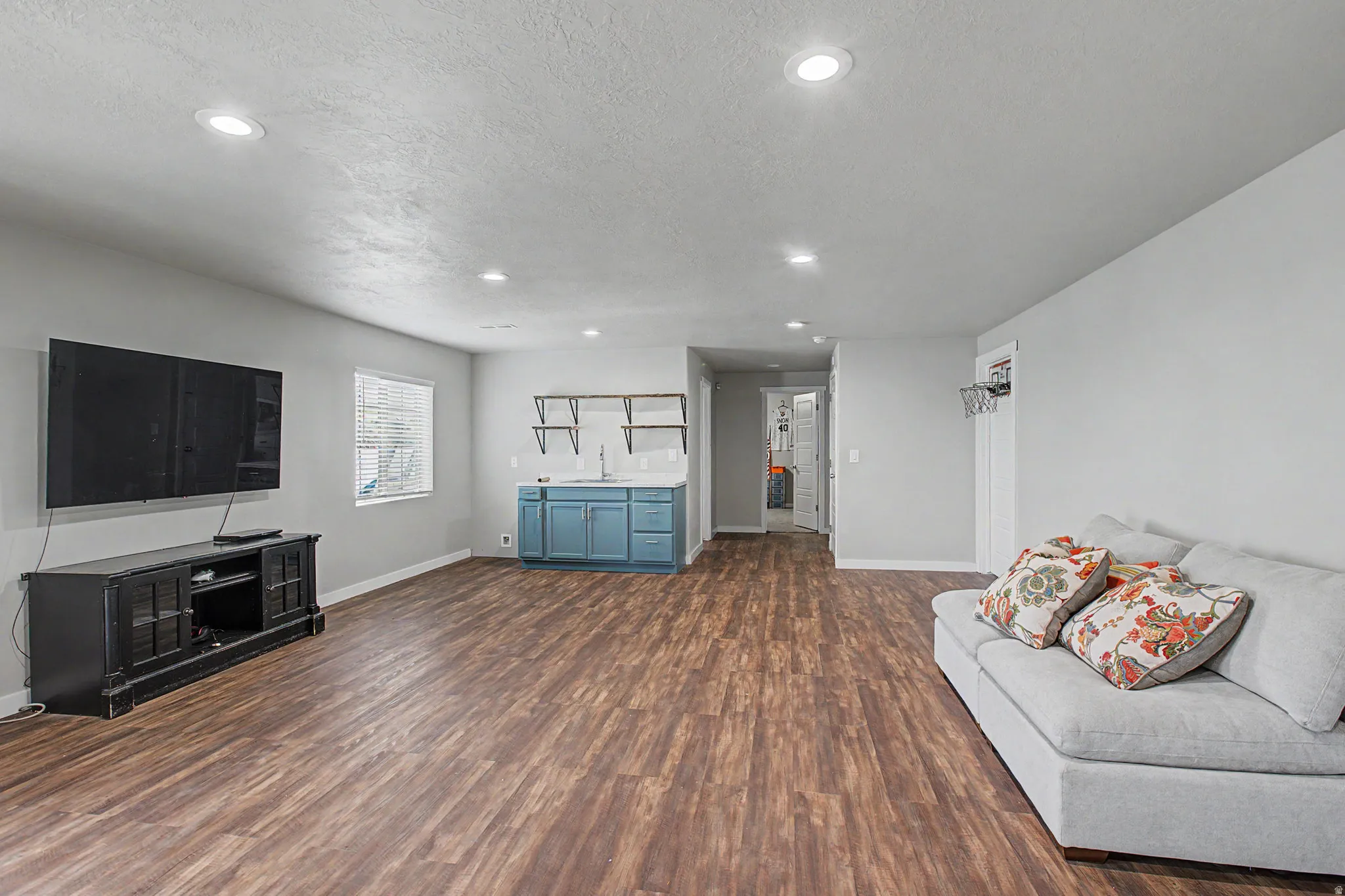 Recessed lighting throughout, wood-finish flooring, a built-in wet bar with a stainless steel sink, and wall-mounted shelving