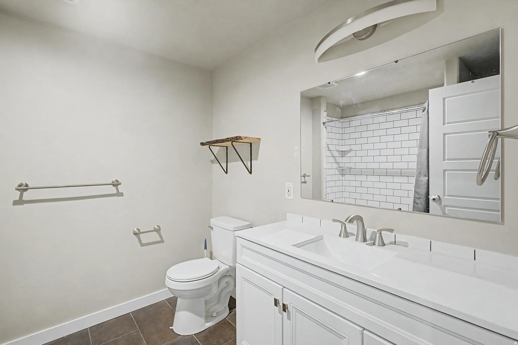 Vanity with integrated sink, subway tile shower surround, wood-finish floating shelf, and dark-toned floor tiles