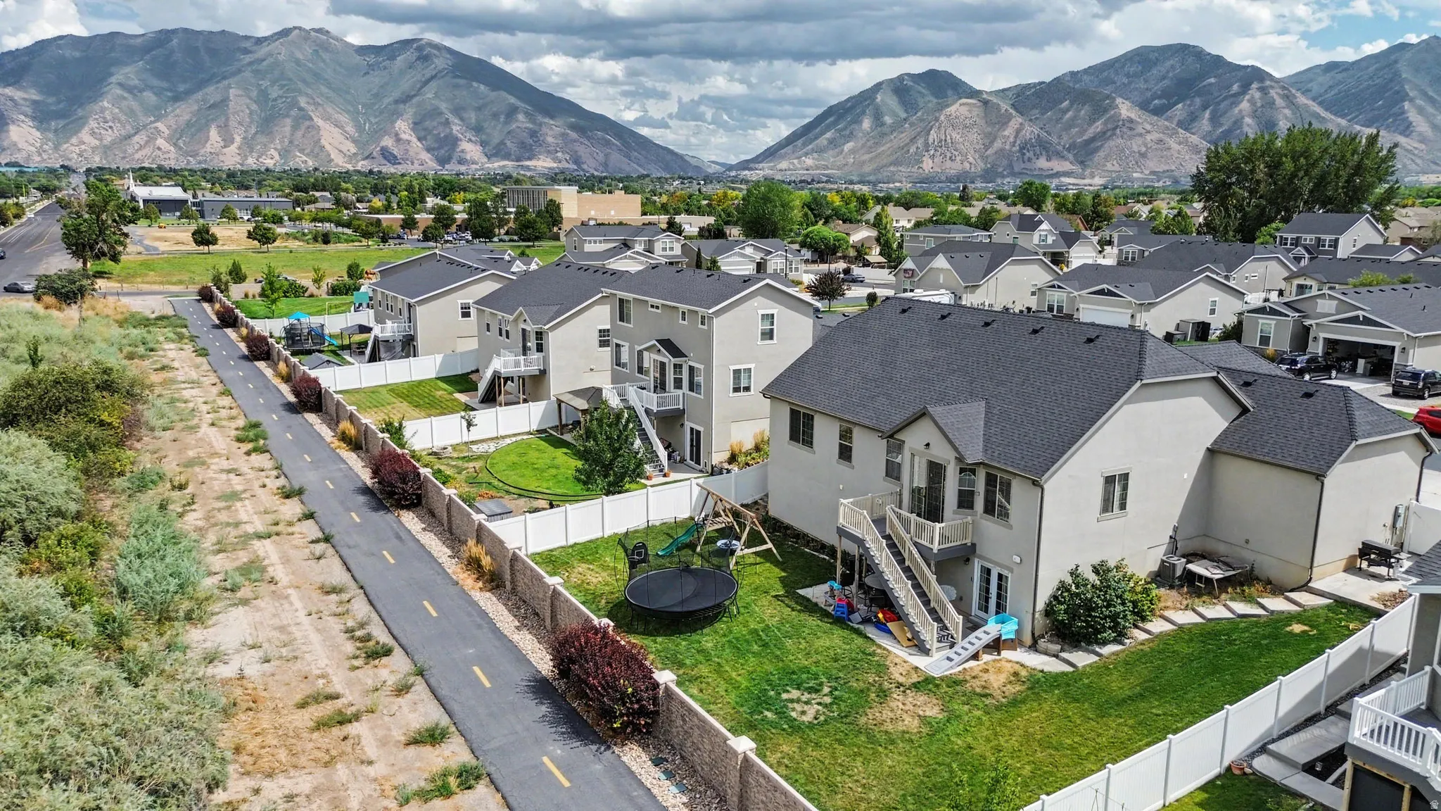 Expansive backyard featuring a manicured lawn, white privacy fencing, and a multi-level deck