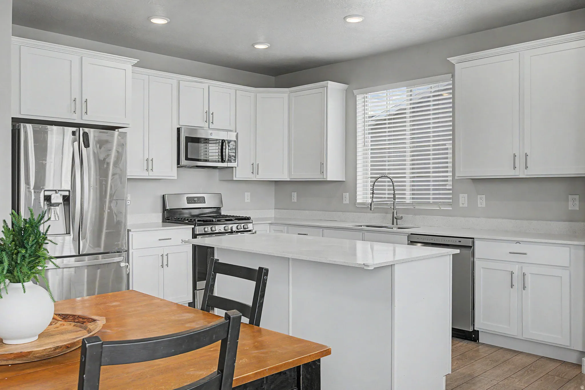 Kitchen with white cabinetry, stainless steel appliances, a center island with a stone-finish countertop, and wood-finish flooring