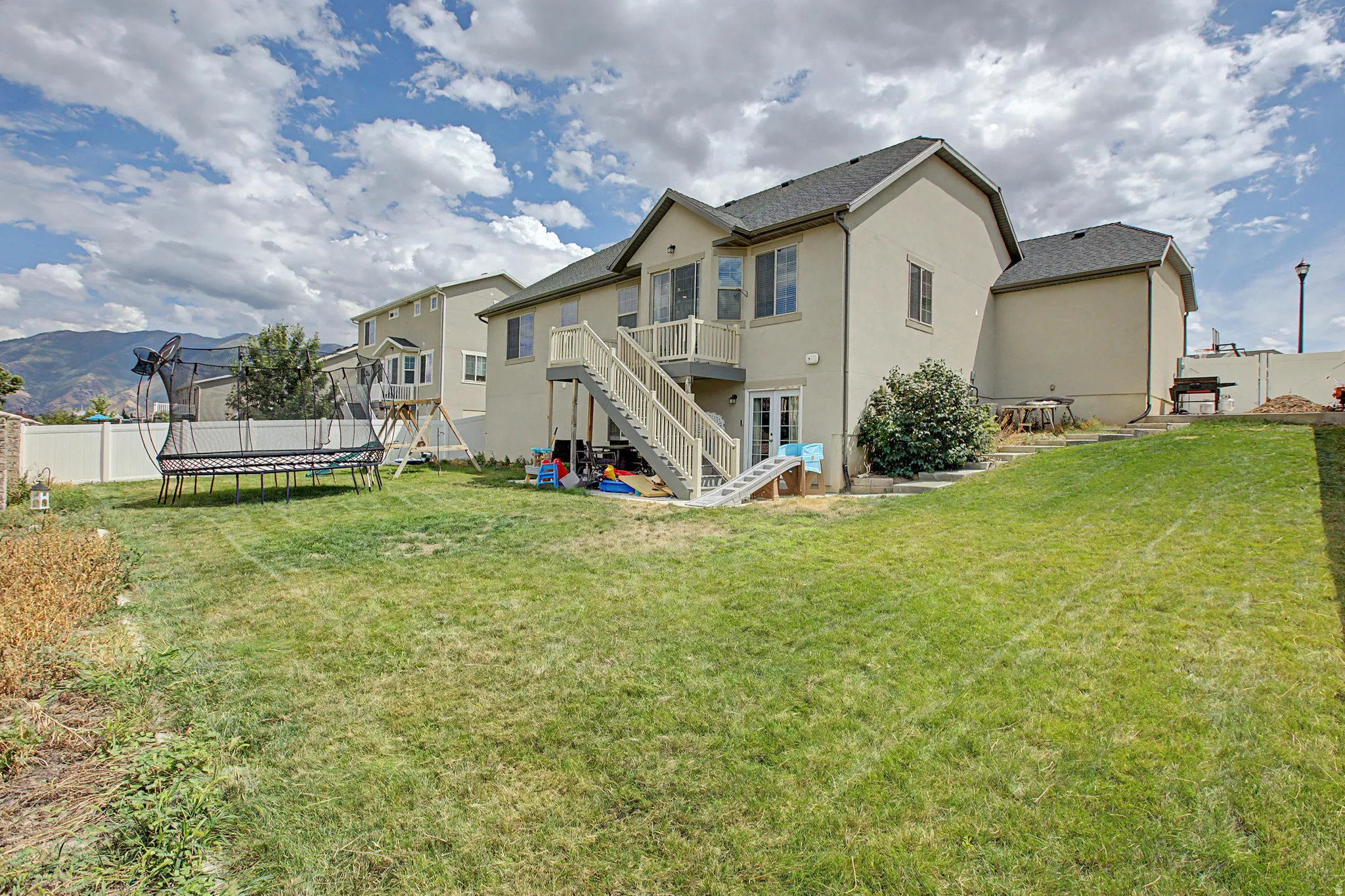 Expansive rear yard featuring a sloped lawn, a multi-story residence with a deck, and double French doors on the lower level