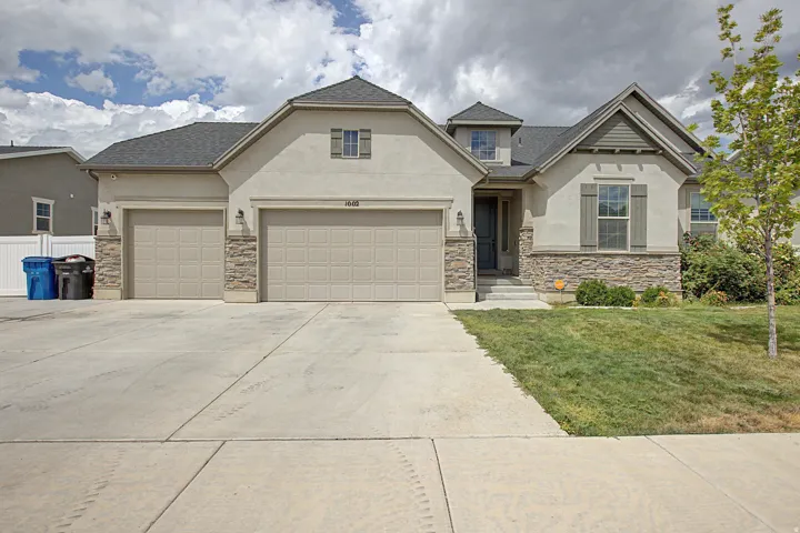 Stucco exterior with stone accenting, dark gray roof, two-car garage, concrete driveway, and established front landscaping