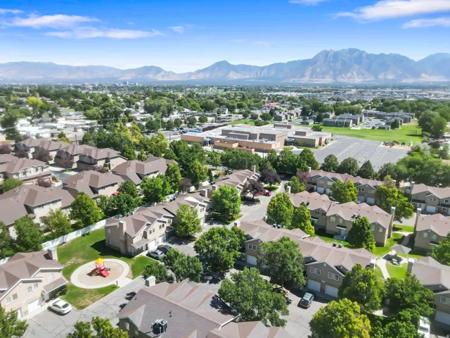 Community aerial featuring townhomes, mature trees, a central playground, and mountain scenery