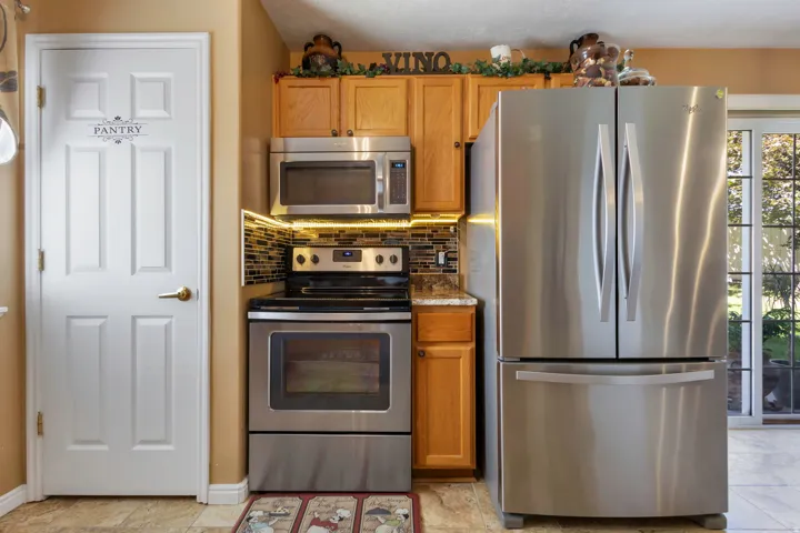 Stainless steel refrigerator and range, wood cabinetry, tile backsplash, and sliding glass door