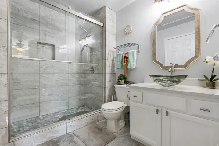 Frameless glass shower enclosure, white vanity with quartz countertop, vessel sink, and rectangular mirror with decorative frame