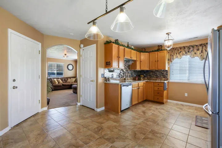 Kitchen featuring tile flooring, wood-finish cabinetry, stainless steel appliances, and a tiled backsplash