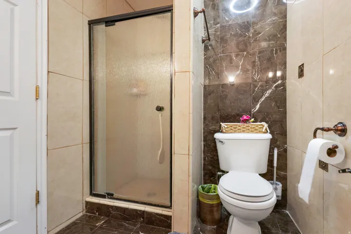 Frosted glass shower enclosure, full wall tiling, modern toilet, and decorative wall sconces