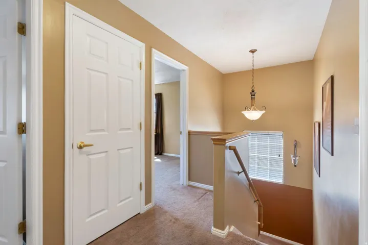 Carpeted hallway with painted walls, white doors, a suspended chandelier, and a wood handrail