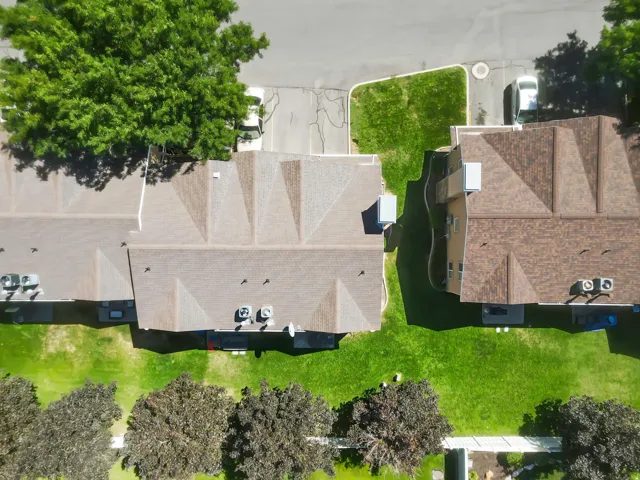 Pitched roofs with shingles, manicured green space, mature trees, paved driveways, and concrete walkways
