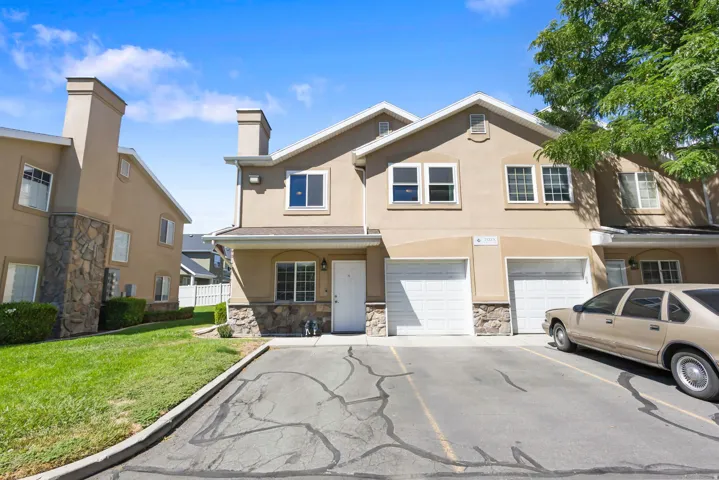 Two-story stucco exterior with stone accents, multiple windows, and two white garage doors