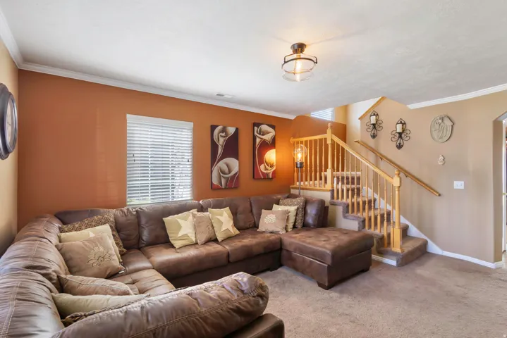 Carpeted flooring, crown molding, double windows with blinds, wood-finish staircase with railing, and a semi-flush mount ceiling fixture
