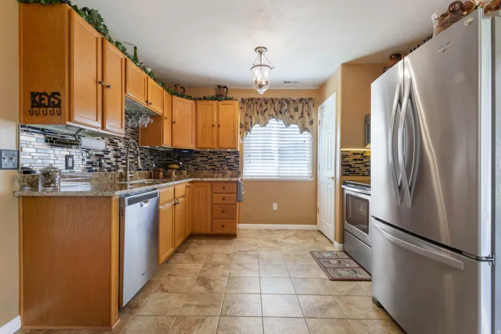 Kitchen featuring wood cabinetry, stainless steel appliances, a tiled backsplash, granite-finish countertops, and tiled flooring