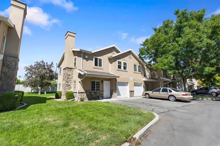 Stucco exterior with stone accents, attached two-car garage, multiple windows, and a prominent chimney feature